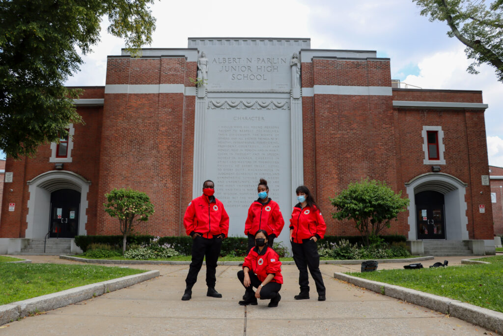 AmeriCorps members in their red City Year jackets gather in front of Albert Parlin School