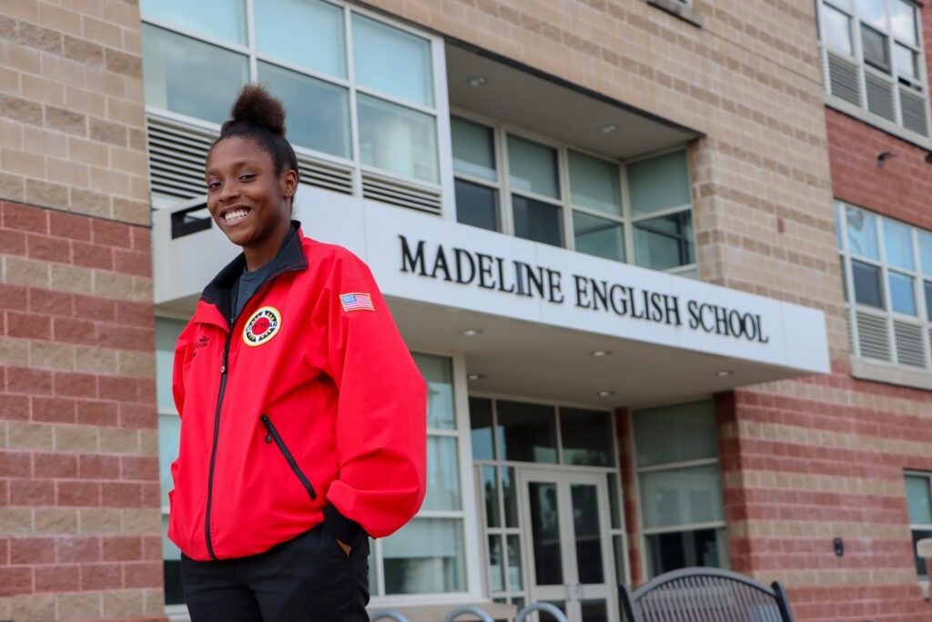 AmeriCorps member in red jacket, smiling in front of Madeline English School