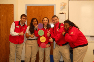 Five City Year AmeriCorps members with their thumbs up in a classroom