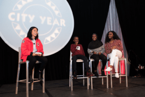 City Year Seattle AmeriCorps member sits on stage with three students at the 2019 Ripples of Hope Gala