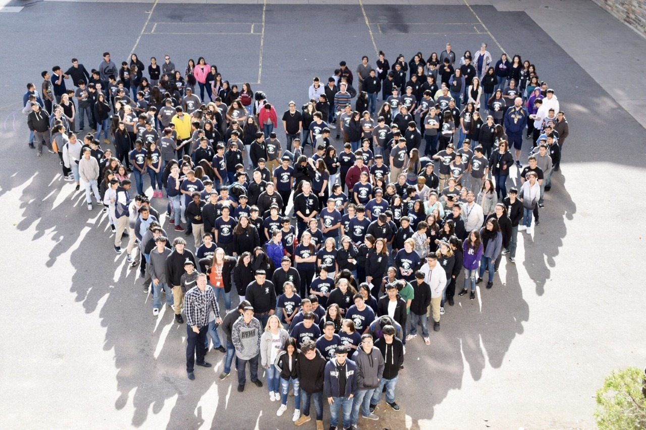 a large group of students a teachers standing in the shape of a filled heart