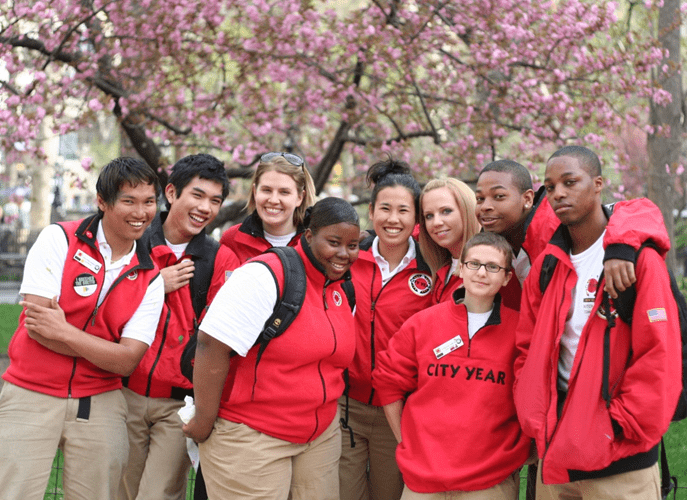 A group of smiling AmeriCorps members pose for a photo in front of cherry blossoms