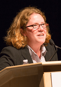 A City Year alum wearing glasses and a black blazor speaks at a podium