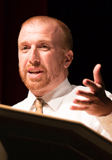 A City Year alum wearing a white button-down shirt speaks at a podium
