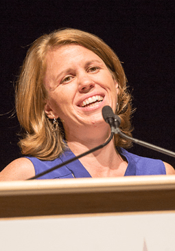 A City Year alum wearing a blue top smiles at a podium