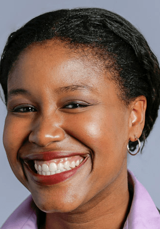 A City Year alum wearing a purple top and silver hoop earrings smiles at the camera