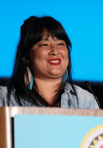 A City Year alum wearing a light denim top and red lipstick speaks at a podium