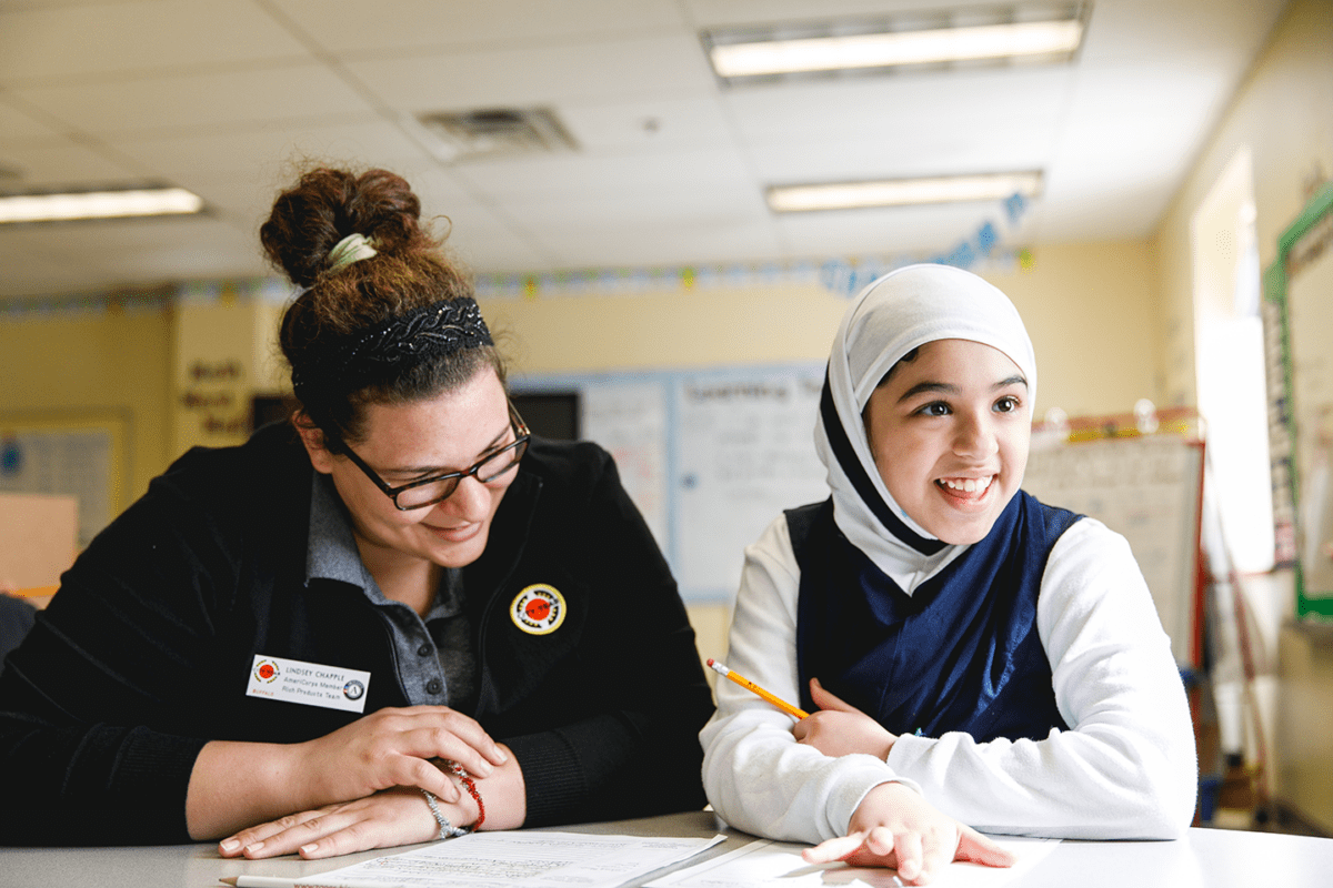 A City Year Buffalo AmeriCorps member and student smile and sit at a table