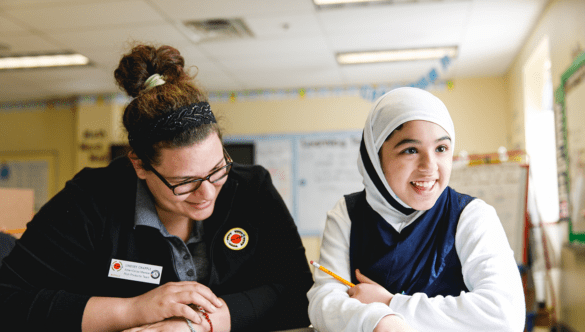 A City Year Buffalo AmeriCorps member and student smile and sit at a table