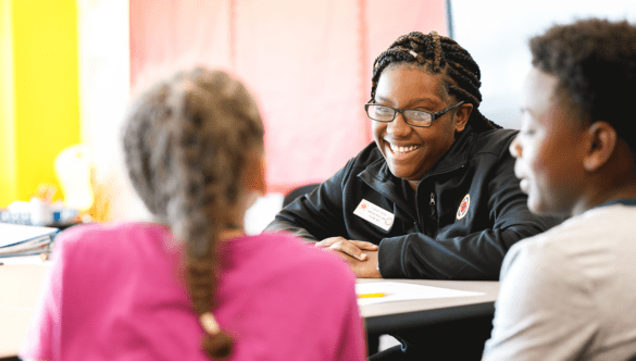 A City Year Buffalo AmeriCorps member laughs and looks across the table at two students
