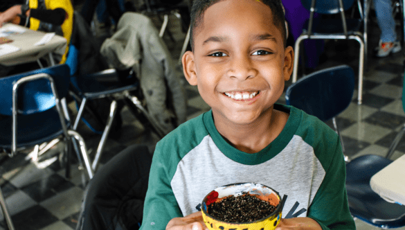 elementary student holds up a plant pot they painted that's filled with soil