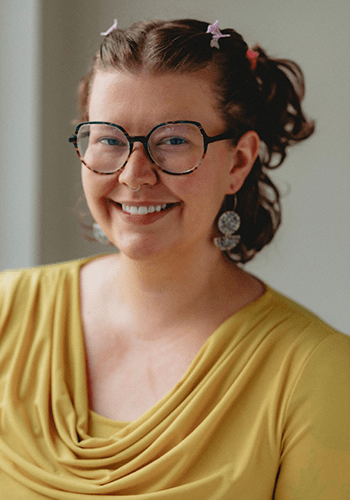 A City Year Milwaukee alum and staff member smiles at the camera in glasses and a yellow blouse