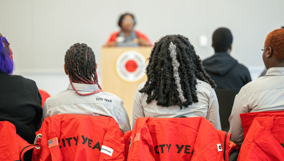 Two City Year Baton Rouge AmeriCorps members sit facing a podium.